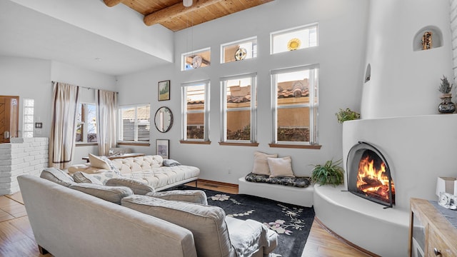 living area with beam ceiling, a towering ceiling, light wood-style floors, wood ceiling, and a warm lit fireplace