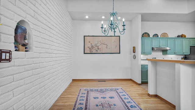 kitchen with light countertops, brick wall, light wood-type flooring, under cabinet range hood, and baseboards