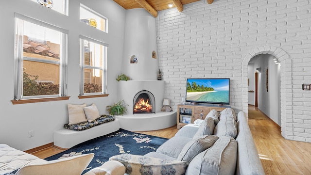 living area with arched walkways, a warm lit fireplace, wood finished floors, wood ceiling, and beam ceiling