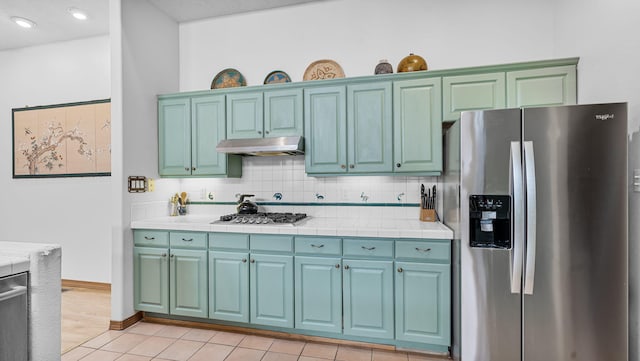 kitchen with tile countertops, backsplash, appliances with stainless steel finishes, light tile patterned flooring, and under cabinet range hood