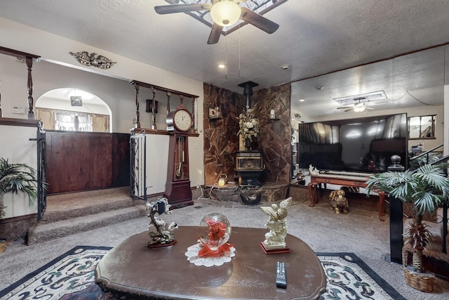 living room with carpet, a wood stove, a textured ceiling, and ceiling fan