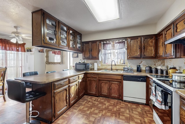 kitchen with a breakfast bar area, white appliances, a textured ceiling, sink, and kitchen peninsula