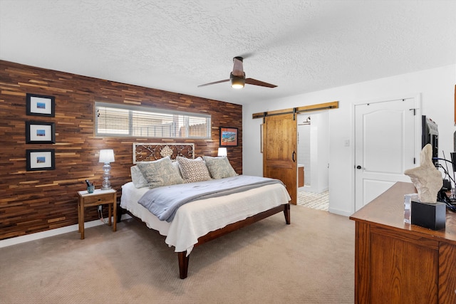 bedroom with a textured ceiling, a barn door, light colored carpet, wood walls, and a ceiling fan