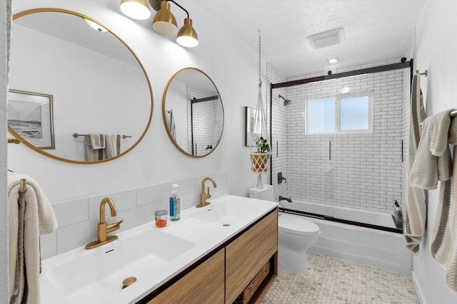 full bathroom with a sink, a textured ceiling, toilet, and bath / shower combo with glass door