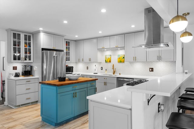 kitchen with island range hood, a sink, wood counters, a kitchen breakfast bar, and appliances with stainless steel finishes