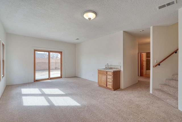 unfurnished room with light carpet, stairway, a textured ceiling, and visible vents