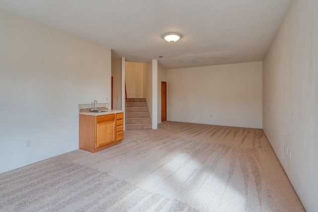 empty room featuring a textured ceiling, stairway, a sink, and light colored carpet