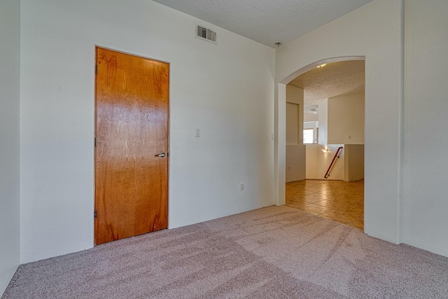 spare room with visible vents, arched walkways, a textured ceiling, and light colored carpet