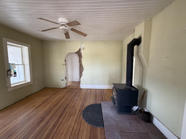 unfurnished living room featuring a wood stove, dark hardwood / wood-style flooring, and ceiling fan