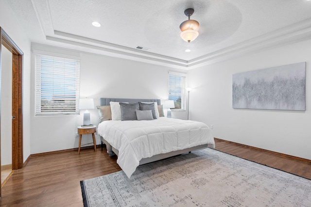 bedroom with a tray ceiling, hardwood / wood-style floors, and a textured ceiling