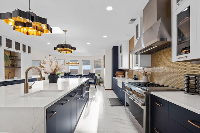 kitchen with sink, hanging light fixtures, wall chimney exhaust hood, stainless steel range, and a large island with sink