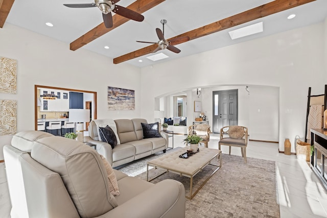 living room featuring beam ceiling, a skylight, ceiling fan, and a high ceiling