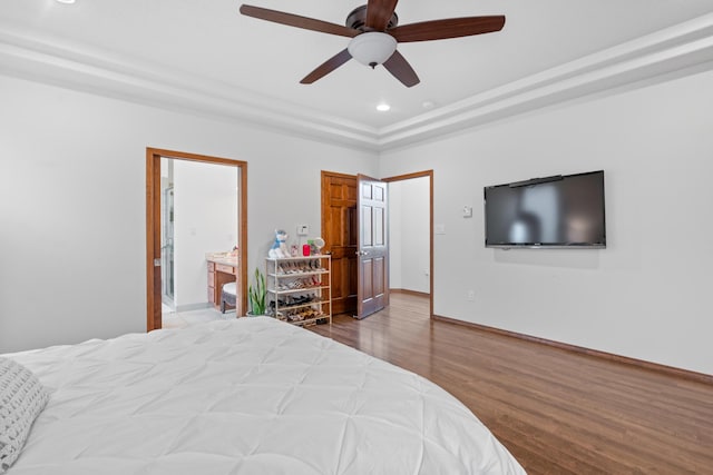 bedroom featuring a tray ceiling, wood-type flooring, ensuite bath, and ceiling fan