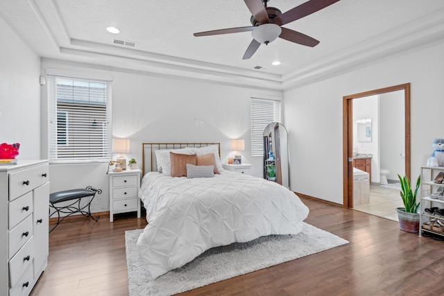 bedroom featuring a raised ceiling, ensuite bathroom, hardwood / wood-style floors, and ceiling fan