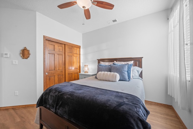 bedroom with a textured ceiling, light hardwood / wood-style floors, a closet, and ceiling fan