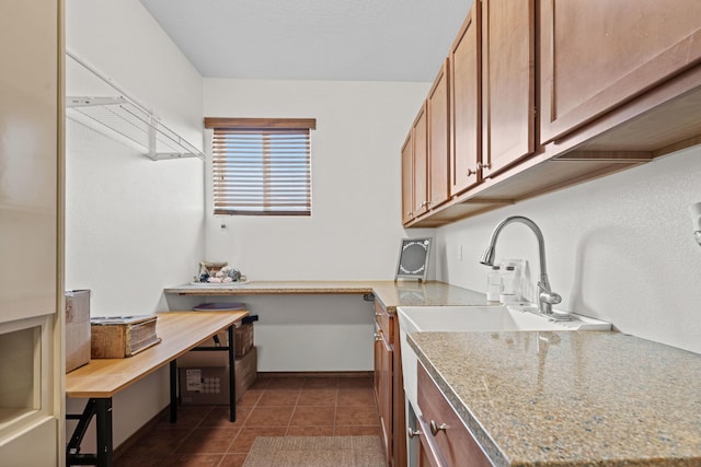 kitchen with light stone counters, dark tile patterned flooring, and sink