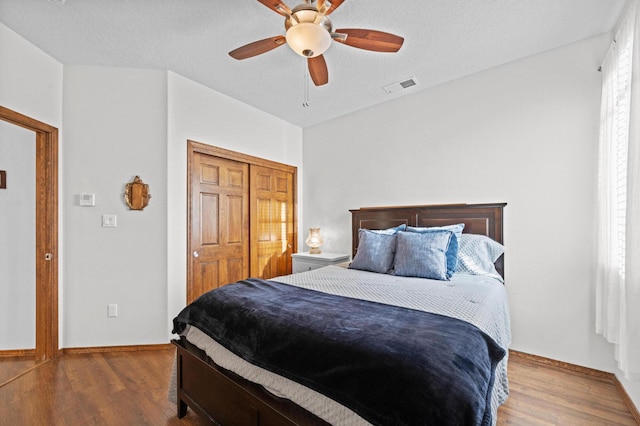 bedroom with hardwood / wood-style floors, a textured ceiling, ceiling fan, and a closet