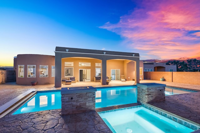 pool at dusk featuring an outdoor living space, a patio area, and an in ground hot tub