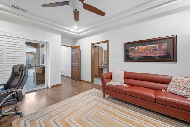 home office with a tray ceiling, ceiling fan, and light wood-type flooring