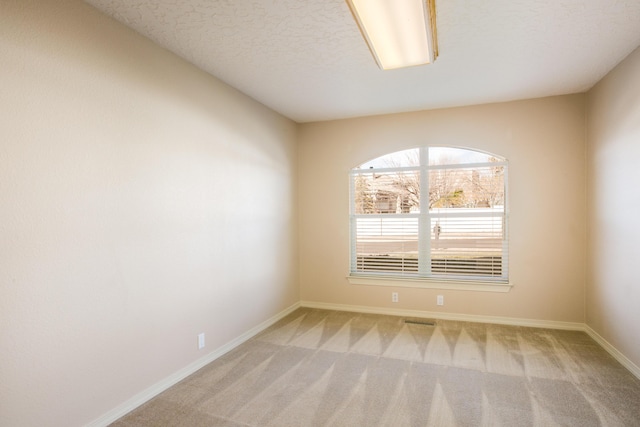 spare room featuring a textured ceiling and light colored carpet