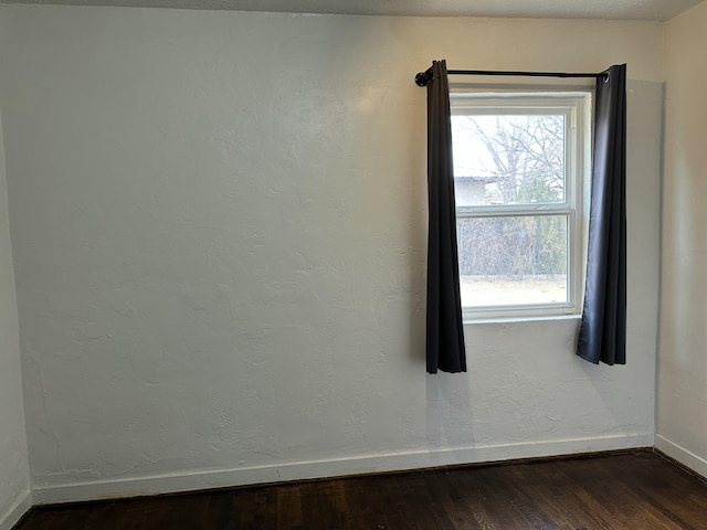 empty room with a healthy amount of sunlight, baseboards, dark wood-style flooring, and a textured wall