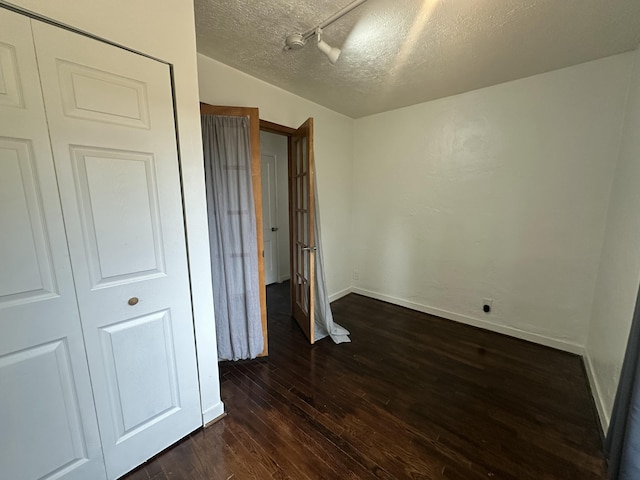 unfurnished bedroom featuring dark wood-style floors, baseboards, and a textured ceiling