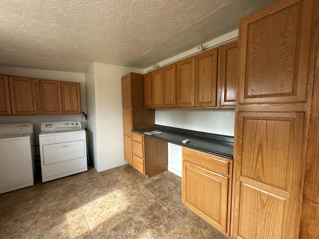 kitchen featuring built in desk, washer and clothes dryer, dark countertops, brown cabinetry, and a textured ceiling