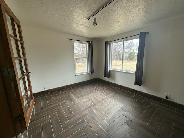 unfurnished room featuring rail lighting, a textured ceiling, and baseboards