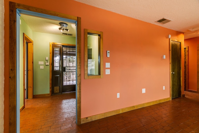 empty room with a textured ceiling, brick floor, visible vents, and baseboards