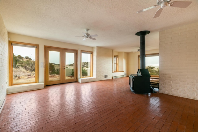 unfurnished living room with ceiling fan, french doors, a wood stove, and a wealth of natural light