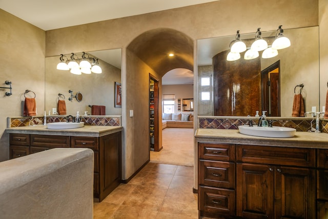 ensuite bathroom with connected bathroom, two vanities, a sink, and backsplash