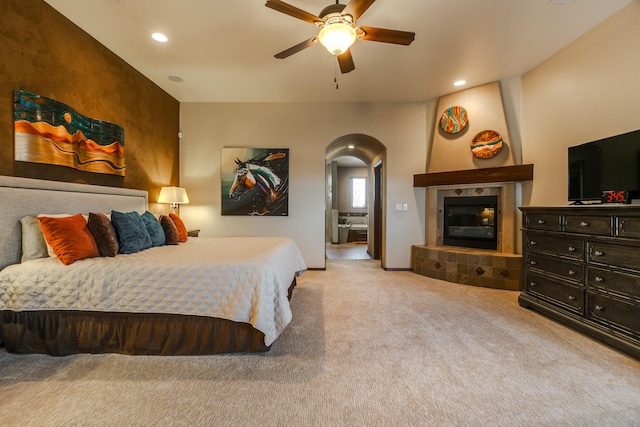 carpeted bedroom featuring a ceiling fan, arched walkways, a tiled fireplace, and recessed lighting