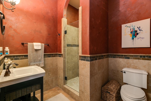 bathroom with wainscoting, toilet, vanity, a shower stall, and tile walls