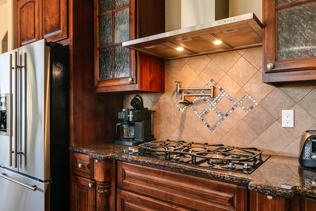 kitchen featuring backsplash, glass insert cabinets, high quality fridge, wall chimney range hood, and black gas stovetop