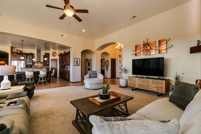 carpeted living room with ceiling fan with notable chandelier, arched walkways, visible vents, and recessed lighting