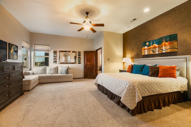 carpeted bedroom featuring ceiling fan, an accent wall, and visible vents