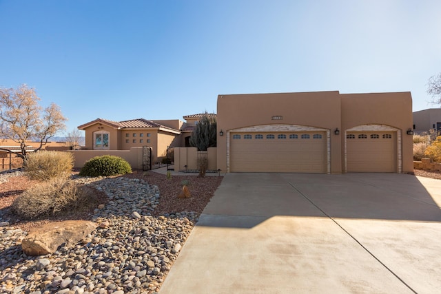 adobe home featuring a garage, concrete driveway, a gate, and stucco siding