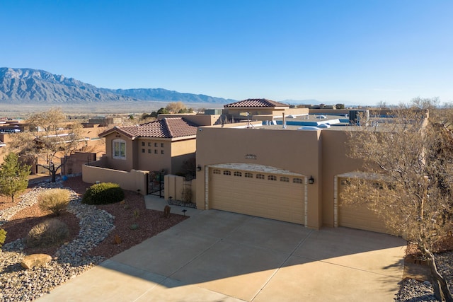 pueblo revival-style home with a garage, concrete driveway, a fenced front yard, a mountain view, and stucco siding