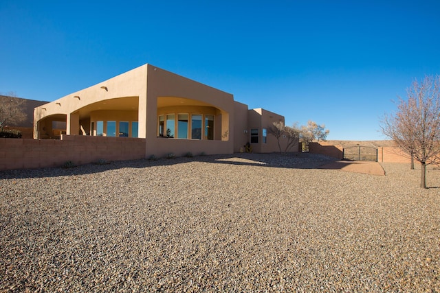 back of property with a gate, fence, and stucco siding