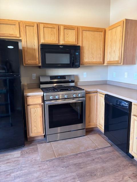 kitchen with light brown cabinets, black appliances, light wood-type flooring, and light countertops