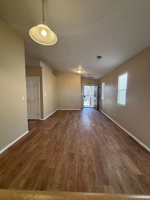 spare room with a textured ceiling, baseboards, vaulted ceiling, and dark wood-style flooring