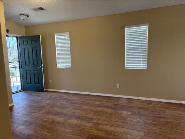 foyer featuring dark wood-style floors, a textured ceiling, visible vents, and baseboards