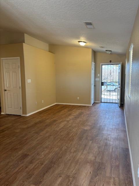 spare room featuring baseboards, visible vents, dark wood finished floors, and a textured ceiling