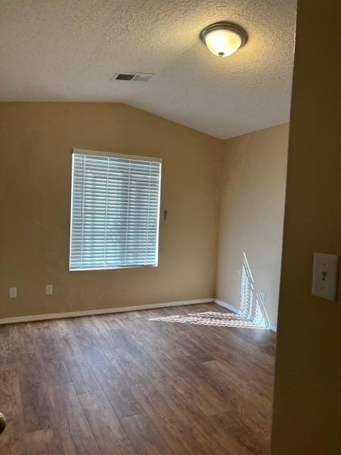 spare room with visible vents, vaulted ceiling, a textured ceiling, wood finished floors, and baseboards