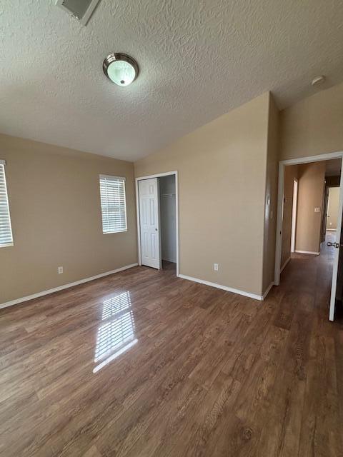 unfurnished room featuring a textured ceiling, visible vents, baseboards, vaulted ceiling, and dark wood finished floors