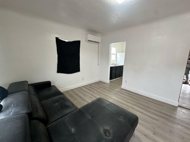 living area featuring light wood-style flooring, baseboards, a textured ceiling, and a wall mounted air conditioner