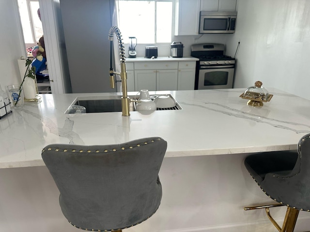 kitchen with stainless steel appliances, light stone counters, a breakfast bar area, and a sink