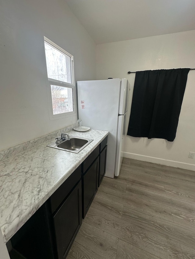 kitchen featuring dark cabinets, freestanding refrigerator, wood finished floors, light countertops, and a sink