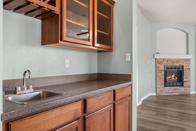 kitchen featuring a fireplace, dark countertops, glass insert cabinets, brown cabinetry, and a sink