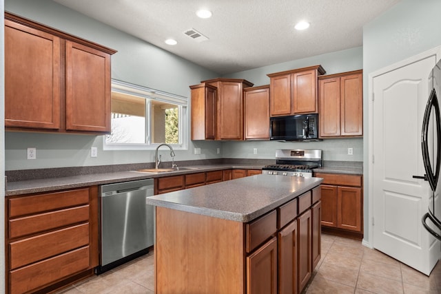 kitchen with visible vents, dark countertops, appliances with stainless steel finishes, a center island, and a sink